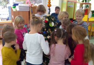 Grupa dzieci ubiera choinkę w sali.
